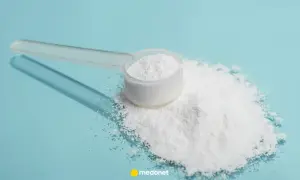 Miarka z białym proszkiem, prawdopodobnie siarka organiczna na stawy, rozsypana na niebieskim tle.