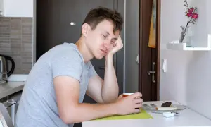 Młody mężczyzna z opartą o dłoń głową, zapatrzony w filiżankę kawy. Nagły spadek energii przyczyny mogą być różne, np. brak snu.