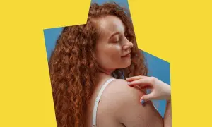 Kobieta z rudymi włosami i piegami dotyka ramienia. Jej skóra lśni, jakby była odżywiona witaminą B7.