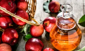 Czerwone jabłka w koszyku i butelka z płynem. Naturalny ocet jabłkowy na zgagę, domowy sposób na ulgę.