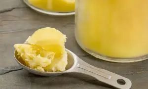 Łyżka z masłem klarowanym, czyli ghee. W tle słoik z tym produktem.