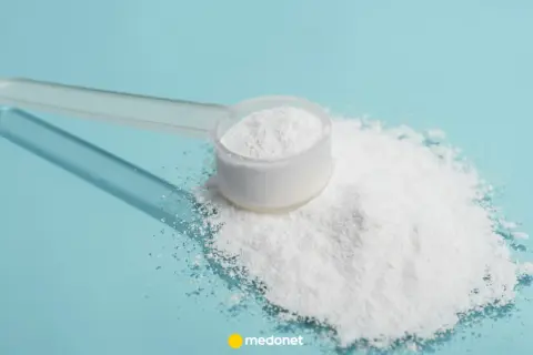 Miarka z białym proszkiem, prawdopodobnie siarka organiczna na stawy, rozsypana na niebieskim tle.