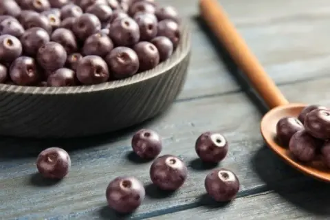 Misternie ułożone owoce acai w misie i na drewnianej łyżce. Zastanawiasz się acai co to? To te ciemne, zdrowe jagody!