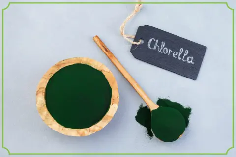 Chlorella tabletki na co pomaga? Zielony proszek w misce i na łyżce, obok tabliczka z napisem "Chlorella".