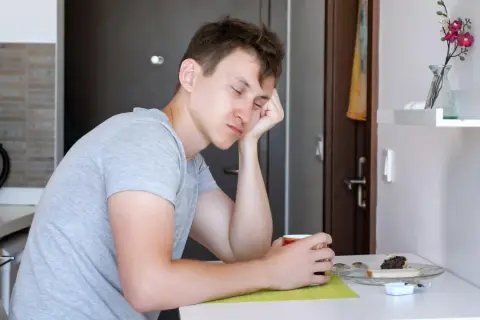 Młody mężczyzna z opartą o dłoń głową, zapatrzony w filiżankę kawy. Nagły spadek energii przyczyny mogą być różne, np. brak snu.
