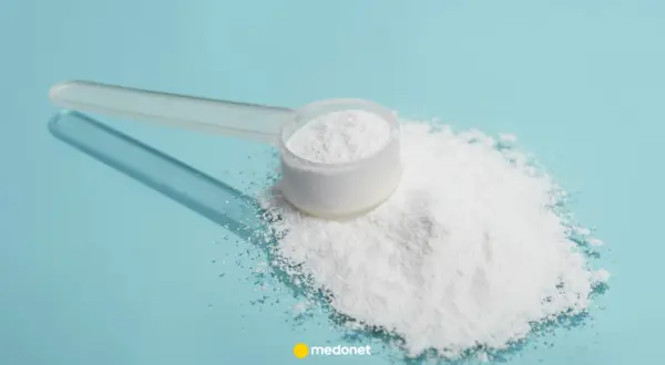 Miarka z białym proszkiem, prawdopodobnie siarka organiczna na stawy, rozsypana na niebieskim tle.