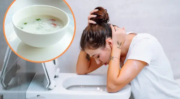 Kobieta z zatruciem pokarmowym pochyla się nad toaletą. Obok miseczka z lekkostrawną zupą, która może pomóc.