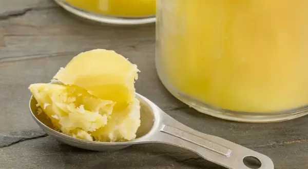 Łyżka z masłem klarowanym, czyli ghee. W tle słoik z tym produktem.