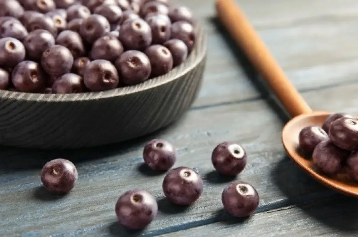 Misternie ułożone owoce acai w misie i na drewnianej łyżce. Zastanawiasz się acai co to? To te ciemne, zdrowe jagody!