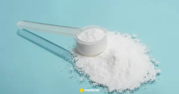 Miarka z białym proszkiem, prawdopodobnie siarka organiczna na stawy, rozsypana na niebieskim tle.