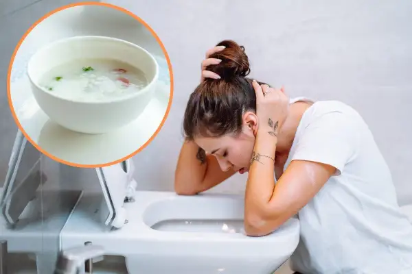 Kobieta z zatruciem pokarmowym pochyla się nad toaletą. Obok miseczka z lekkostrawną zupą, która może pomóc.