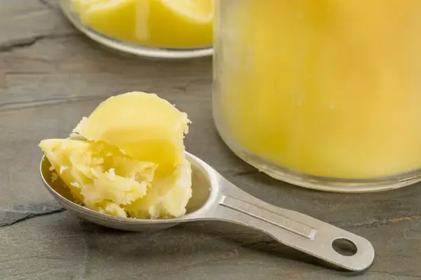 Łyżka z masłem klarowanym, czyli ghee. W tle słoik z tym produktem.